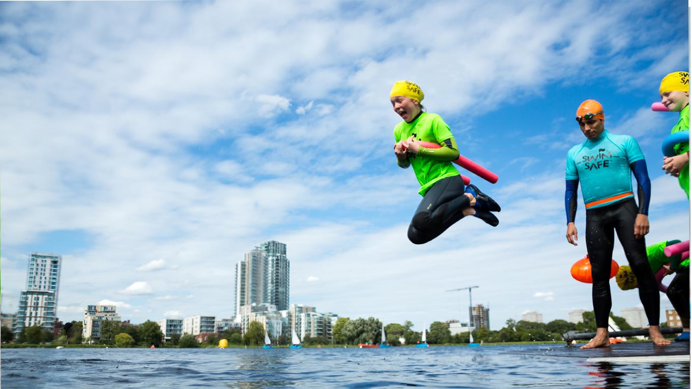 A young girl taking part in Swim Safe a water safety session jumps into West Reservoir in Stoke Newington, London